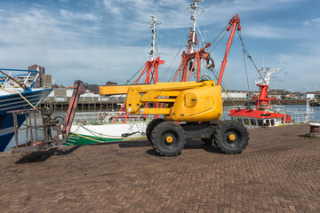 yellow mobile crane with passenger box is outside on the quay of the port