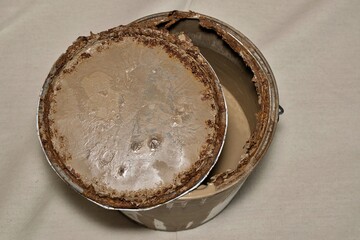 Rusted old metal paint tin with open lid on drop cloth brown expired storage concept.