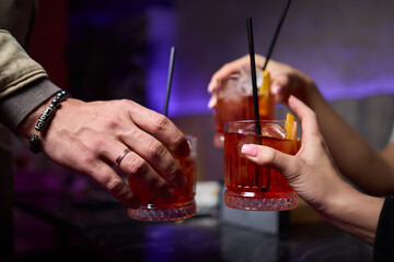 A woman holds a cocktail in her hand, with her fingers wrapped around the glass