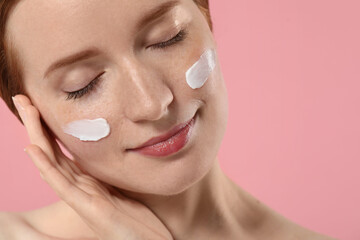Obraz premium Beautiful woman with freckles and cream on her face against pink background, closeup. Space for text