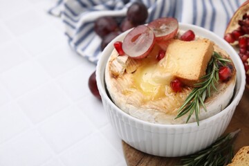 Tasty baked camembert with crouton, grape and rosemary on white tiled table, closeup. Space for text