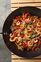 Shrimp stir fry with vegetables in wok on grey table, top view