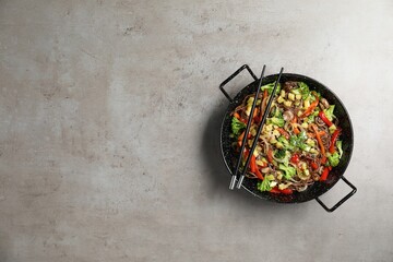 Stir-fry. Tasty noodles with meat in wok and chopsticks on grey textured table, top view. Space for text