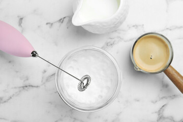Flat lay composition with mini mixer (milk frother), whipped milk in glass and coffee at white marble table