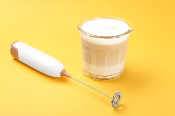 Mini mixer (milk frother) and tasty cappuccino in glass on yellow background © New Africa
