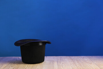 Magician's hat on wooden table against blue background, space for text