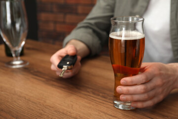 Man with glass of alcoholic drink holding car key at table, closeup. Don't drink and drive concept