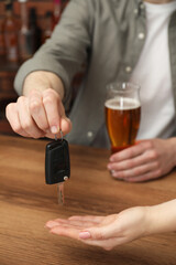 Man with glass of alcoholic drink giving car key to woman at table, closeup. Don't drink and drive...