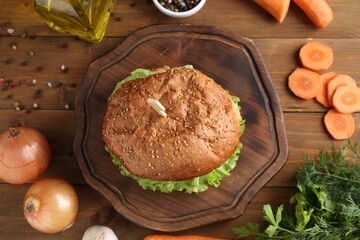 Delicious vegetarian burger and ingredients on wooden table, flat lay