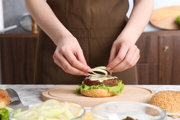 Woman making delicious vegetarian burger at white marble table, closeup