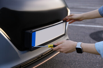 Woman with screwdriver installing vehicle registration plate to car outdoors, closeup