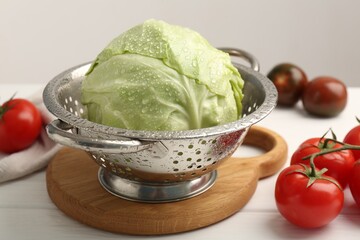 Wet cabbage in colander and tomatoes on white wooden table, closeup