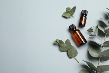 Aromatherapy. Bottles of essential oil and eucalyptus leaves on light grey background, flat lay....