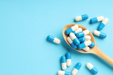 Many antibiotic pills with wooden spoon and space for text on light blue background, top view....