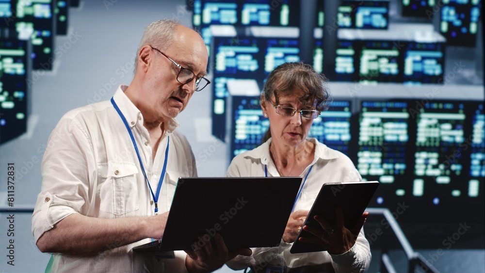 Poster knowledgeable it practitioners looking around server farm, using laptop and tablet to crosscheck dis