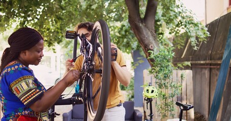In the yard active sports-loving boyfriend and girlfriend changing bicycle tire with work tools for...