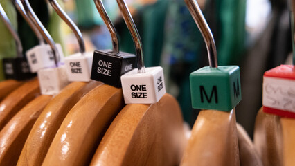 Close up of wooden clothes hangers with coloured size cubes for medium and one size in a retail...