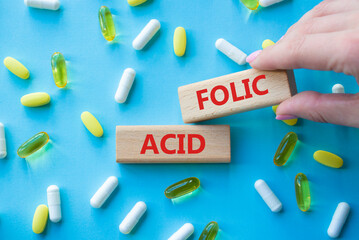 Folic acid symbol. Wooden blocks with words Folic acid. Beautiful blue background with pills....