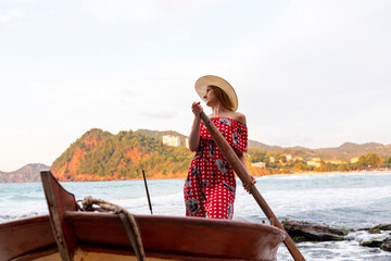 A woman in a red polka dot dress is rowing a boat on a sea.