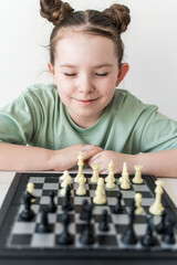 Cute little girl sitting in front of a chessboard with a cunning look. Selected focus.