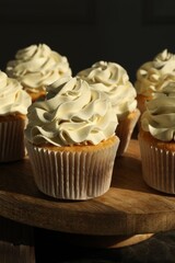 Tasty cupcakes with vanilla cream on wooden stand, closeup