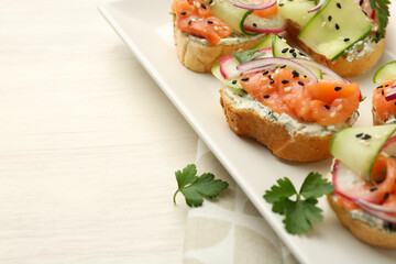Tasty canapes with salmon served on white wooden table, closeup. Space for text