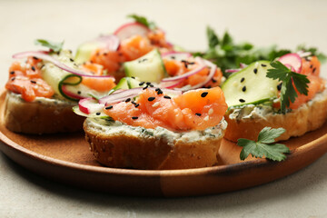 Tasty canapes with salmon served on light grey table, closeup