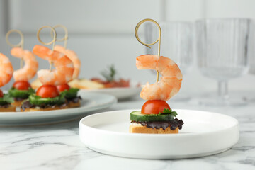 Tasty canapes with shrimps, cucumber, greens and tomatoes on white marble table