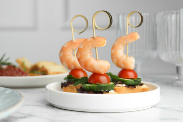 Tasty canapes with shrimps, cucumber, greens and tomatoes on white marble table, closeup