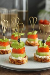 Tasty canapes with salmon, cucumber, bread and cream cheese on wooden table, closeup