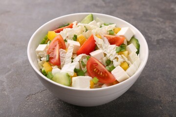 Tasty salad with Chinese cabbage, tomato, cheese, pepper and cucumber on grey table