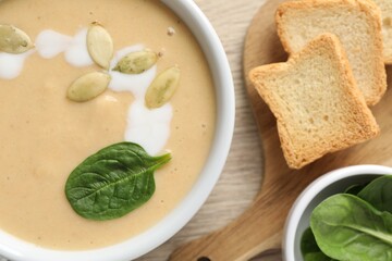 Healthy cream soup high in vegetable fats, bread and spinach on wooden table, flat lay