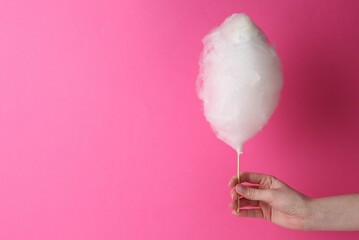 Woman holding sweet cotton candy on pink background, closeup. Space for text