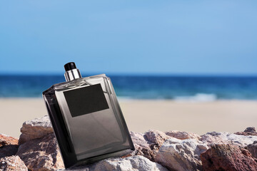 Bottle of aquatic perfume on stones near ocean. Fresh sea breeze scent