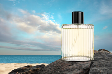 Bottle of aquatic perfume on rock near ocean. Fresh sea breeze scent