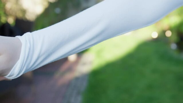 Slow motion macro shot of a person pulling the sleeve of the shirt over the thumb as a tick prevention measure. Person preventing to get bitten by a tick during summer.  