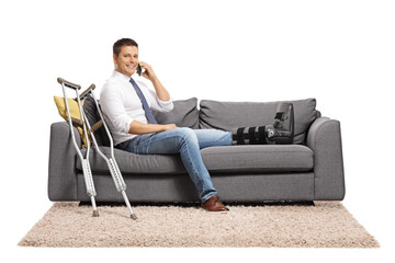 Businessman with a foot injury and leg brace sitting on a sofa and using a smartphone