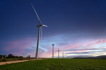 A photo of a wind farm and it's turbines during the sunrise with soft clouds and dramatic colors 