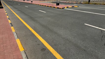 An empty curving auto road with distinct yellow restriction lines, white lane markings and a...