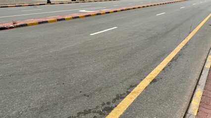 An empty curving auto road with distinct yellow restriction lines, white lane markings and a...