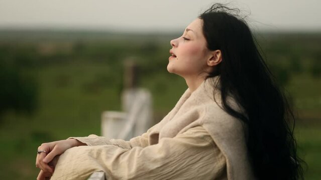 Portrait of calm young woman looking ahead and exhaling fresh air taking deep breath and reducing stress after hard dat at countryside Serene dark haired female resting for peaceful mind outdoors