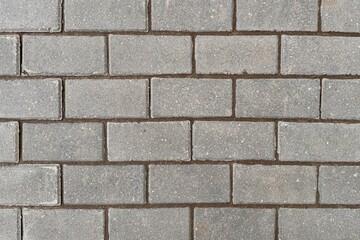 Detailed closeup of a grey rectangular brick wall showing intricate brickwork pattern. Made of composite material resembling concrete. Ideal for road surface or flooring design