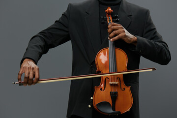 Elegant African American man in black suit holding a violin on gray background for music concept