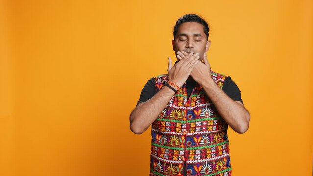 Man wearing traditional indian clothing covering eyes, ears and mouth, imitating three wise monkeys, doing dont see, dont hear and dont speak hand gesturing concept, studio background, camera B