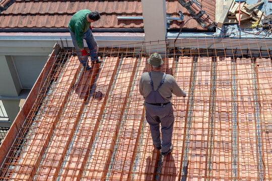 Construction workers prepare a steel mesh to reinforce a roof slab extension before pouring a concrete mix.