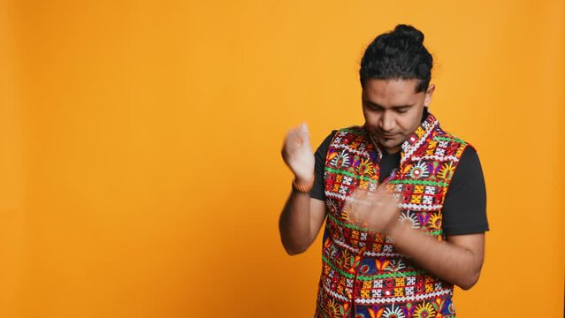 Indian man covering face with palms in disbelief, feeling upset by events, isolated over studio background. Gutted person clawing nails on skin in frustration, irked by troubling news, camera B