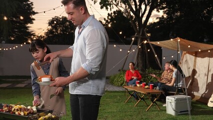 Family celebrate holiday in garden, Father and child grill food for family member. Outdoor camping...