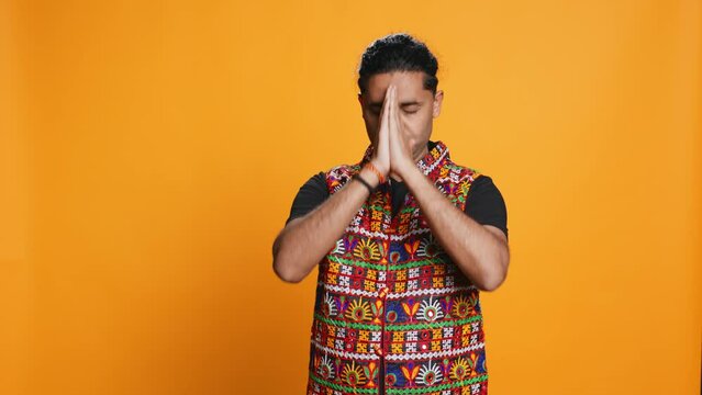 Indian man putting hands together in begging gesture, making wish, isolated over studio background. Faithful person asking for something, praying and hoping, believing in higher power, camera B