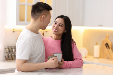 Lovely couple with cups of drink enjoying time together in kitchen, space for text