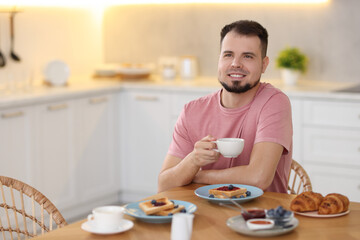 Smiling man drinking coffee at breakfast indoors. Space for text